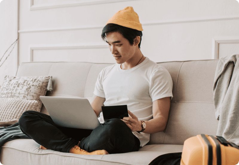 Man wearing a yellow hat sitting on the couch signing up for expat insurance with his laptop