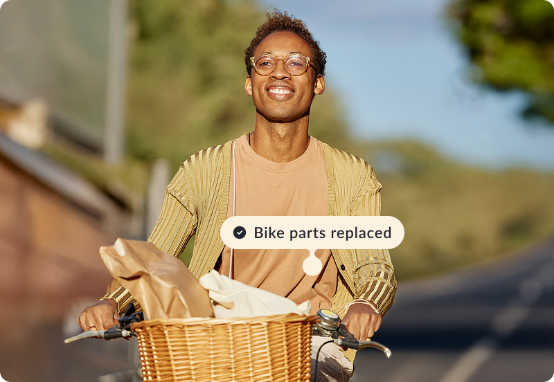 Person riding a bicycle, smiling on a sunny road. A label reads 'Bike parts replaced'.