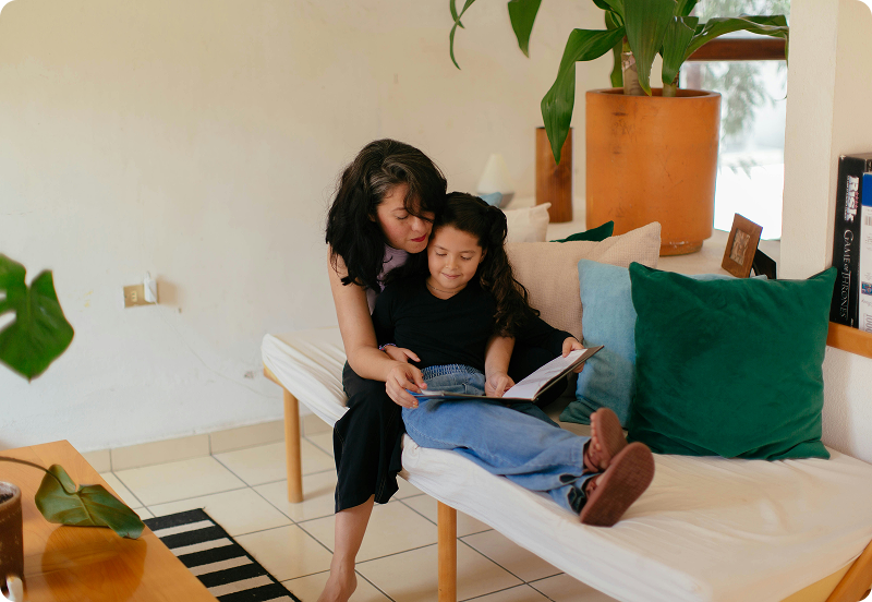 Mother and daughter sitting on a couch reading a book together.