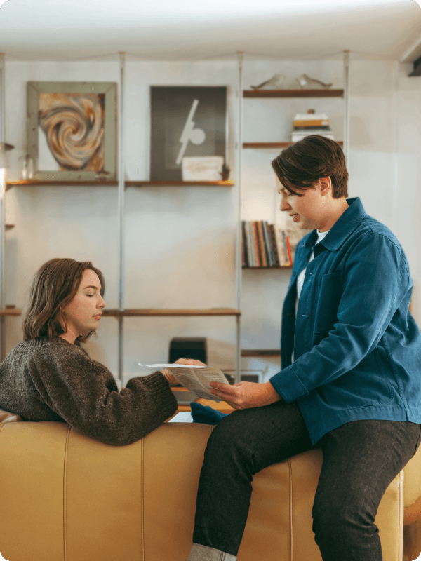 Two people sitting in a living room, looking at documents and talking.