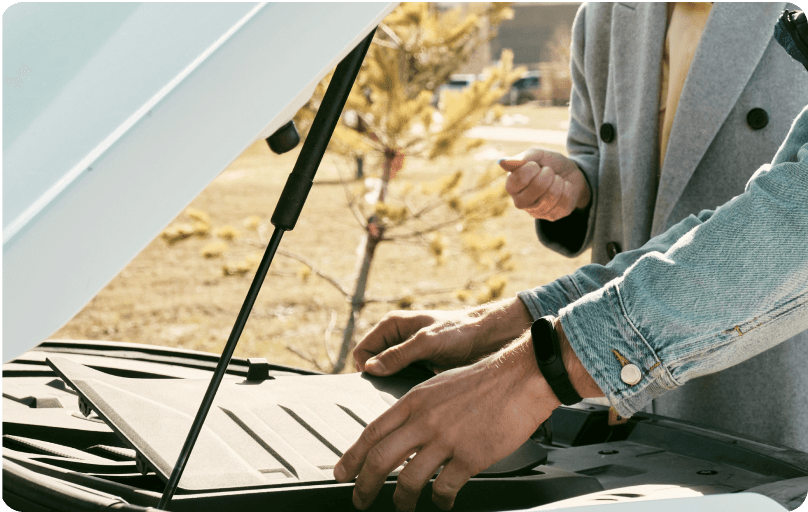 A car with opened front bonnet and two people checking a car engine.