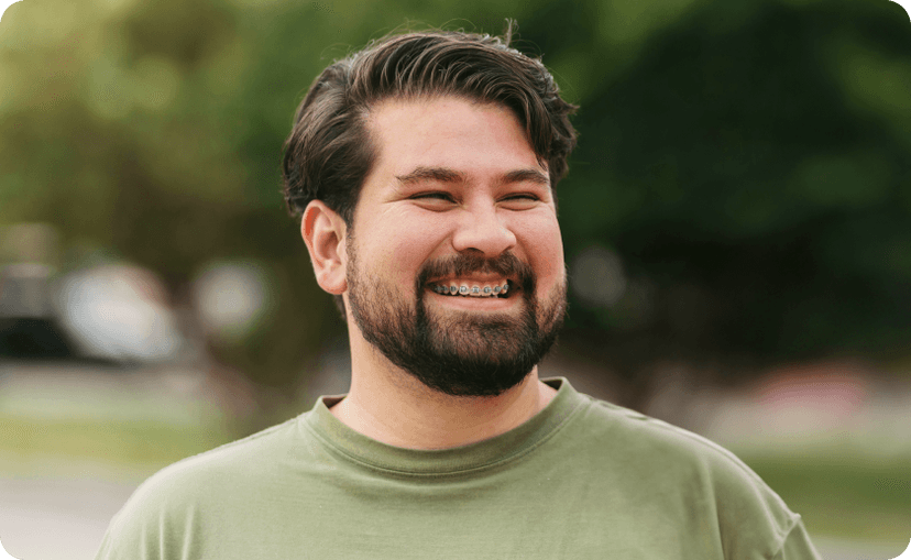 Portrait of a man in a park smiling with braces on his teeth.