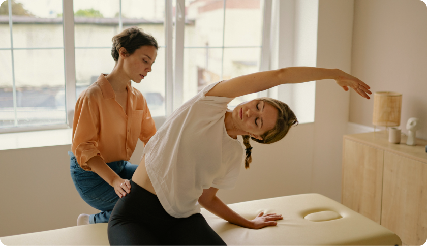 Person in a doctor's office doing back stretch exercise while being assisted by their doctor.