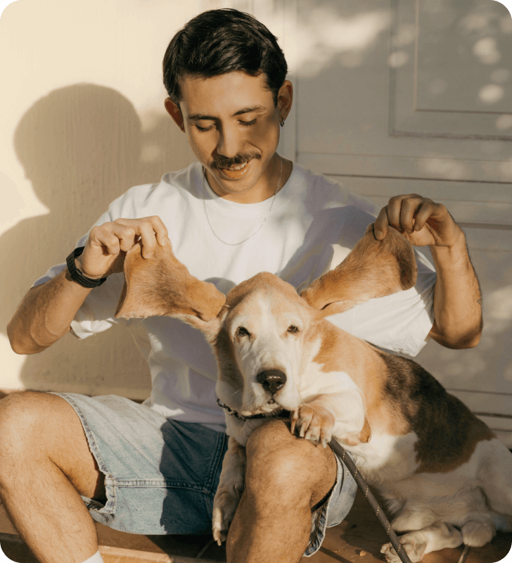 Person sitting outside with their dog, smiling and playing with dog's ears.