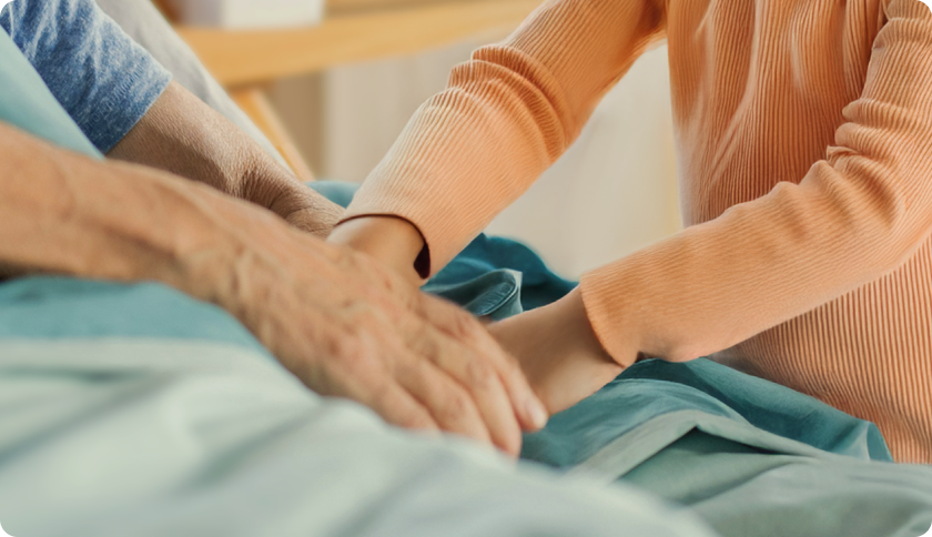 Older man laying on a hospital bed, holding hands with his granddaughter.