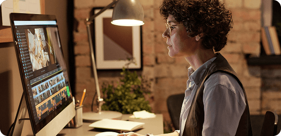 A woman working at her desk, in front of a computer screen, editing a video.