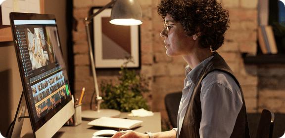 A woman working at her desk, in front of a computer screen, editing a video.