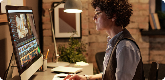 A woman working at her desk, in front of a computer screen, editing a video.