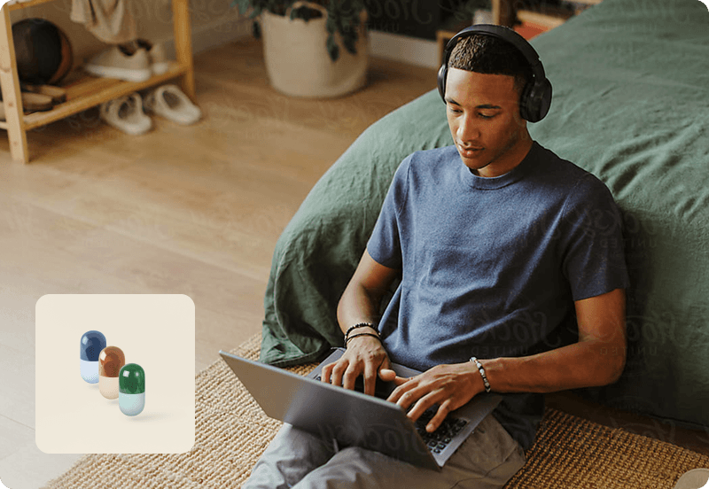 Man looking at his laptop, sitting on the carpet in his bedroom.