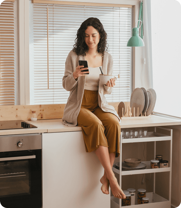 A picture of a person that sits on their kitchen table with a cup of coffee and a phone.