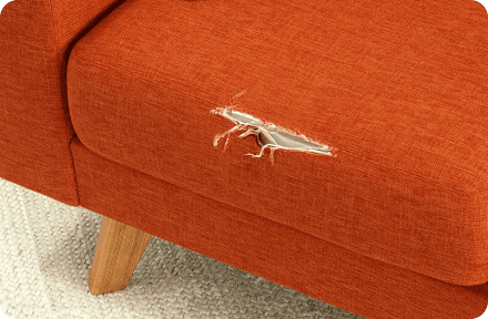 An orange couch with a hole in the fabric pillow.