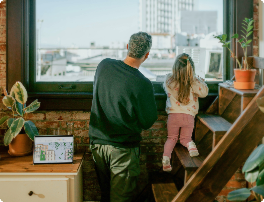 Father and a daughter looking through a window in their cozy apartment showing sky and city buildings.