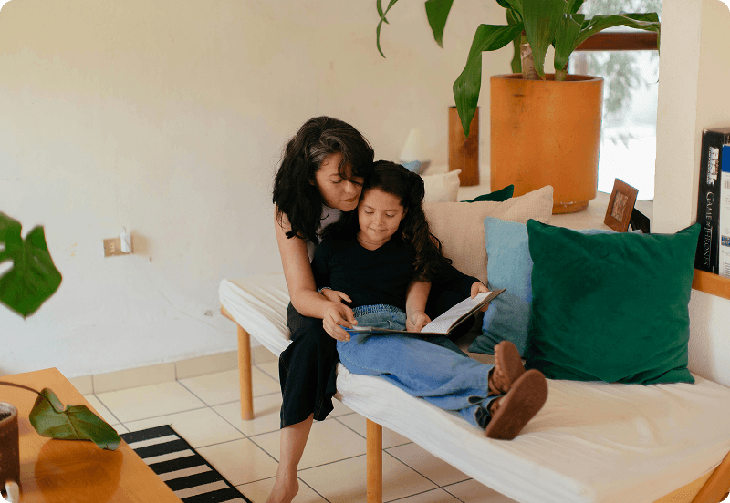 A woman sitting on a couch with her daughter, and reading her a book in Bulgaria.