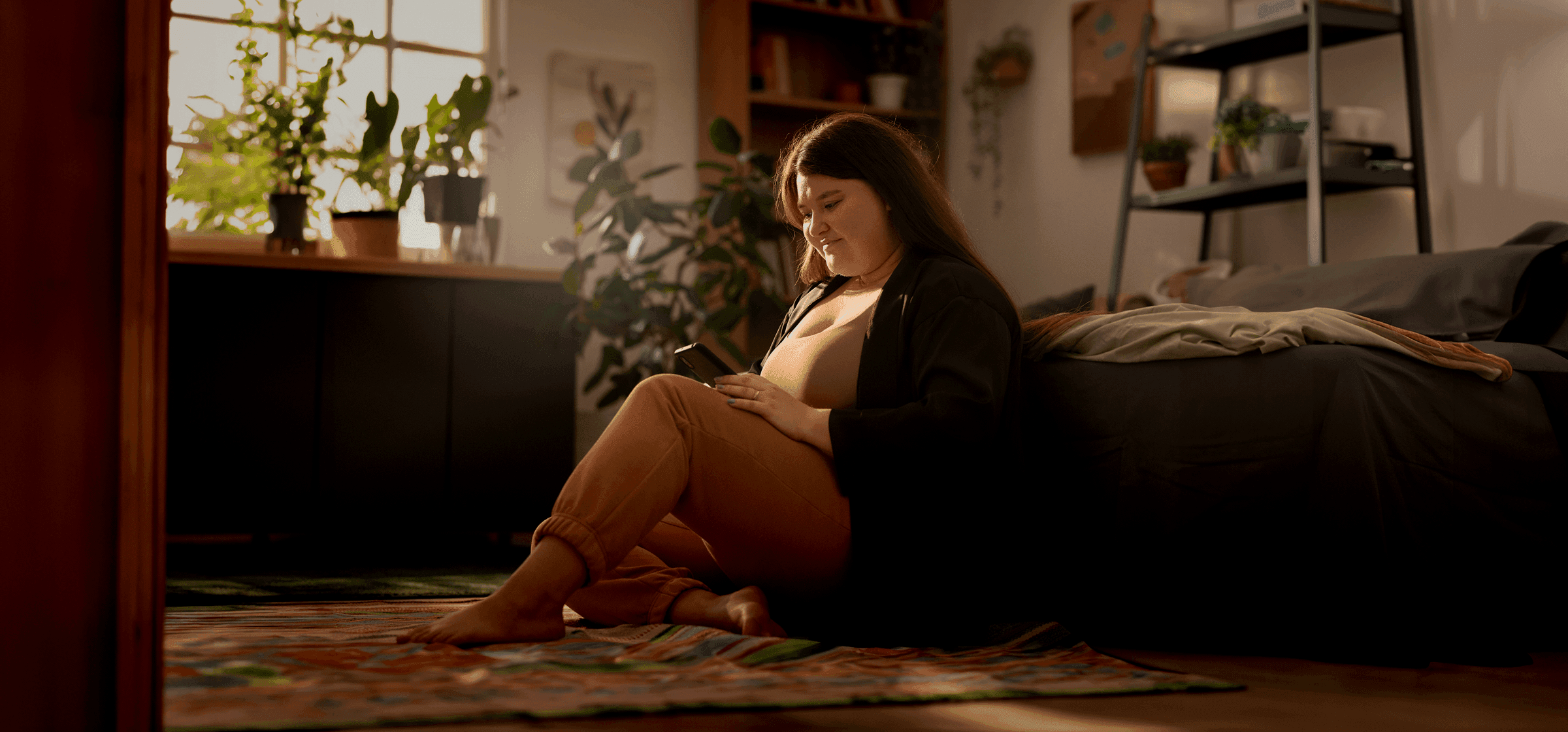A woman sitting on the floor of her sunlit apartment, relaxed and looking at her phone."