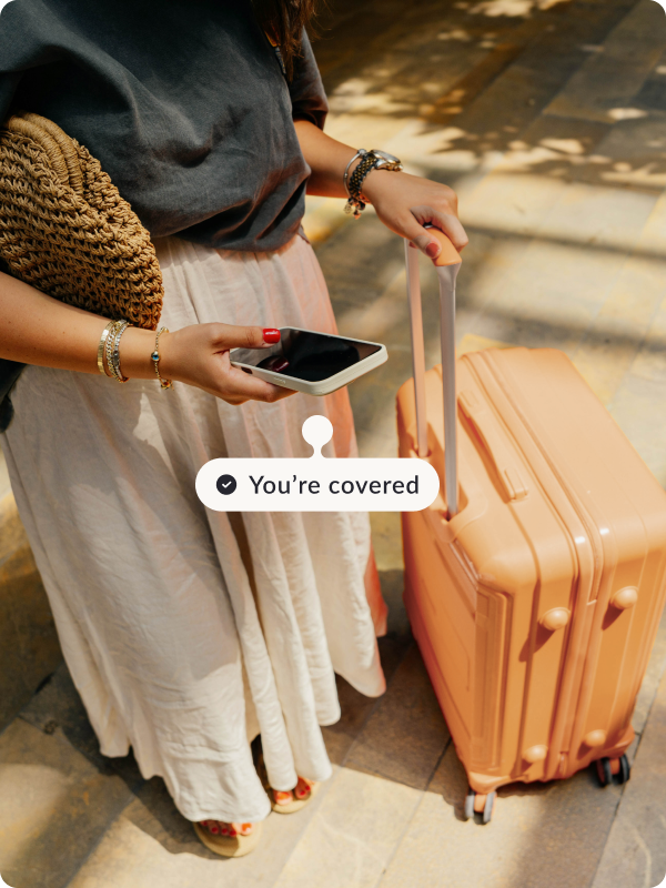 Person holding their suitcase and looking at a phone. The tag next to the phone reads "You're covered".